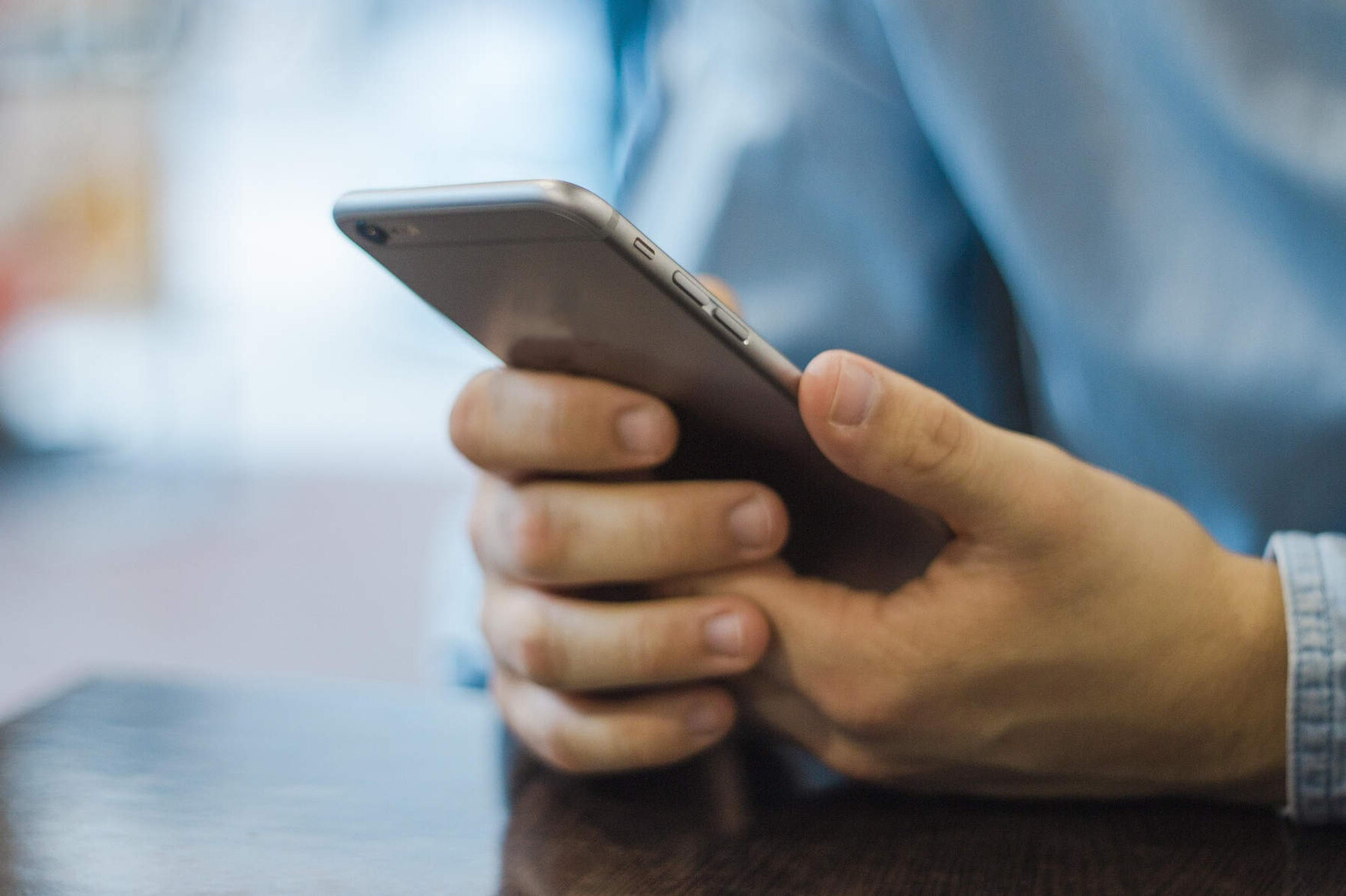 Die Hände eines Mannes halten ein Handy. Der Betrachter schaut von hinten auf das Handy. Die rechte Hand des Mannes tippt mit dem Daumen etwas auf dem Display.